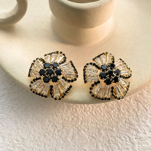 Close-up of gold flower earrings with black gemstone centers and zircon petals