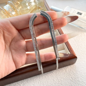 Close-up of long silver fringe earrings with rectangular zircons in a handheld view