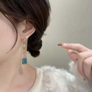 Dettaglio degli orecchini con pietra blu rettangolare e zirconi trasparenti su modella