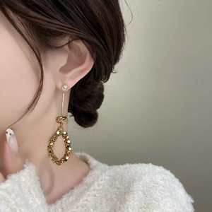 Dettaglio di lunghi orecchini a goccia dorati con paillettes e strass su una modella