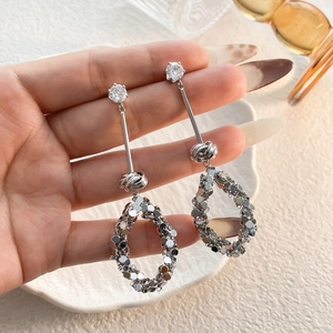 Dettaglio ravvicinato di orecchini lunghi in argento con zircone e paillettes metalliche