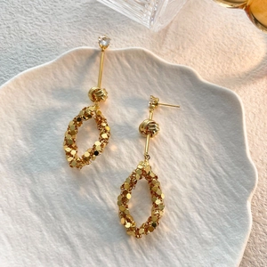 Dettaglio di orecchini pendenti in oro con paillettes ovali e zircone su ceramica