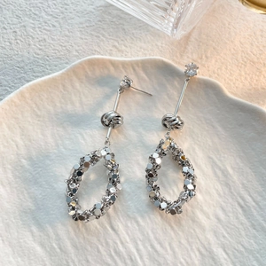 Dettaglio di orecchini a pendente in argento con paillettes e zirconi su ceramica