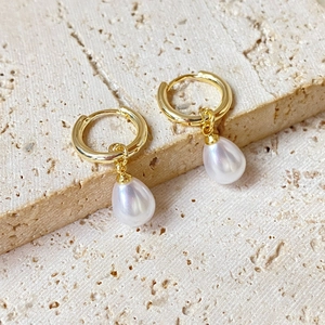 Elegant gold hoop earrings with white teardrop pearl pendants on a textured stone surface