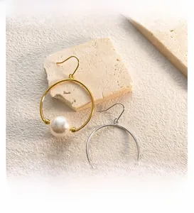 Detailed close-up of 18K gold and silver pearl drop earrings on a stone texture background