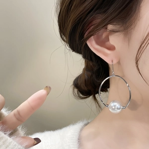 Minimalist silver hoop earrings with a large white pearl drop on a female model