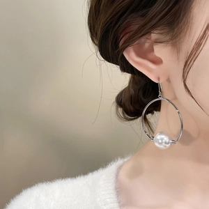 Close-up of a silver metal hoop earring with a large white pearl on a model's ear