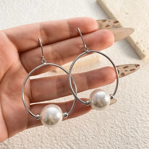 Macro detail of elegant large hoop earrings featuring white pearls and 18K gold plated finish