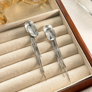 Detail view of silver tassel drop earrings featuring textured metal on a velvet display