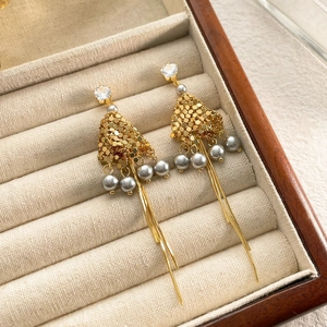 Dettaglio di orecchini a nappa dorati con perle e strass su espositore in velluto beige