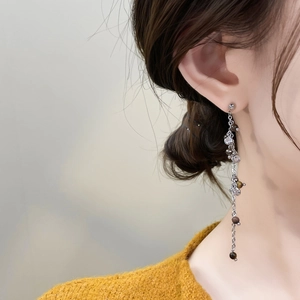 Detail of long tassel earrings with zircon beads worn on a yellow sweater model