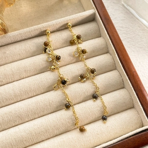 Detail of long gold tassel earrings with brown beads and zircon on a jewelry box