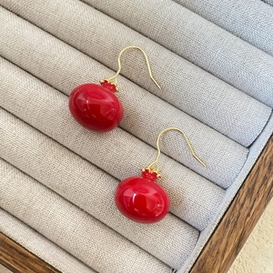 Elegant red pomegranate drop earrings with gold hooks on a beige jewelry display