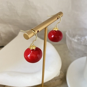 Macro detail of red festive drop earrings with golden hollow filigree caps on a T-stand