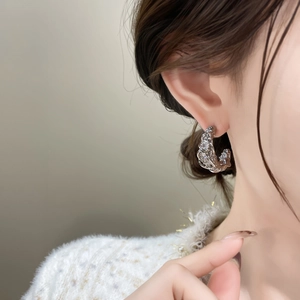 Dettaglio degli orecchini a torsione con strass su giacca in tweed bianca