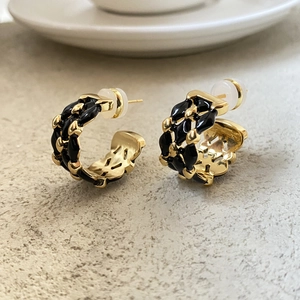 Close-up of C-shaped black and 18K gold-plated lattice earrings on a textured stone