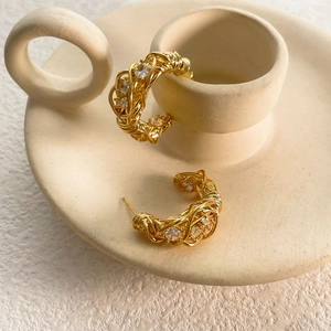 Dettaglio di orecchini a C placcati in oro 18k con metallo intrecciato e zirconi chiari