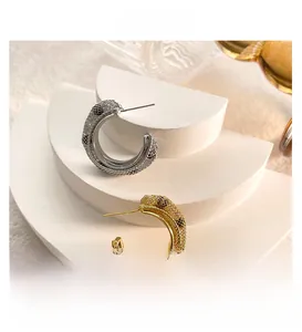 Detail view of gold and silver C-shaped mesh woven earrings on a white geometric stand