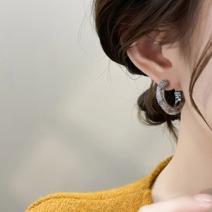 Detail of silver C-shape earring with textured finish on a model wearing a yellow sweater