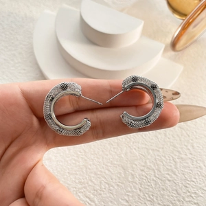 Macro detail of silver-tone C-shaped hoop earrings with intricate woven mesh texture