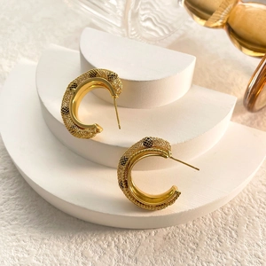 Close-up of C-shaped gold mesh earrings displayed on white geometric steps with soft light