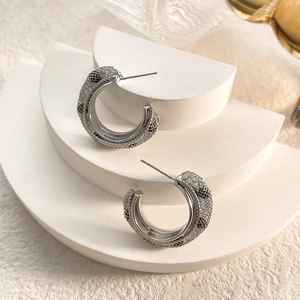 Detailed view of silver mesh hoop earrings on a white minimalist display stand
