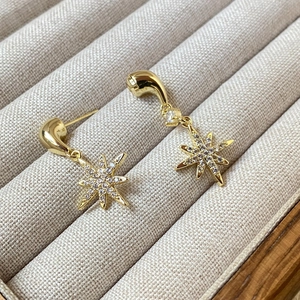Macro detail of gold eight-pointed star earrings with shimmering pavé zircon stones