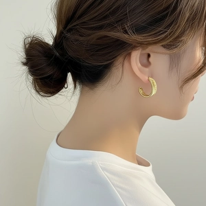 Detalle de pendientes de aro de metal trenzado bañados en oro de 18K con textura mate fina