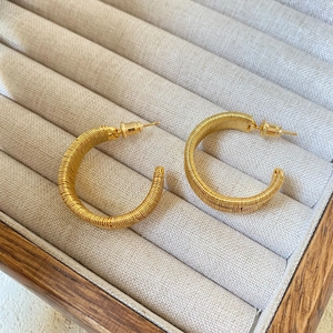 Elegantes pendientes de aro trenzados bañados en oro de 18K sobre bandeja de joyería beige