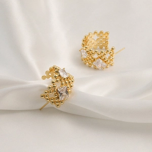 Macro detail of gold C-shape geometric earrings with square zircons on white silk