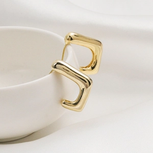 Boucles d'oreilles créoles carrées dorées minimalistes polies sur une tasse en céramique