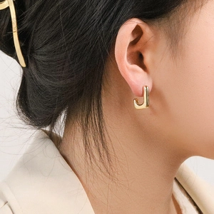 Boucles d'oreilles géométriques dorées en forme de J portées par un mannequin chic