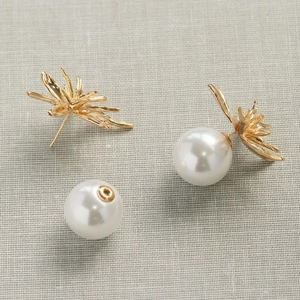 Detail of gold flower earrings with large pearl jacket backings on linen background