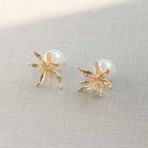 Detailed close-up of gold flower pearl earrings on a textured linen background