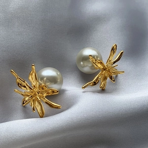 Exaggerated geometric metal flower earrings with pearls on elegant silk fabric background