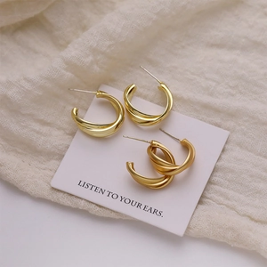 Three-layer twisted metal C-shaped gold hoop earrings on textured white background