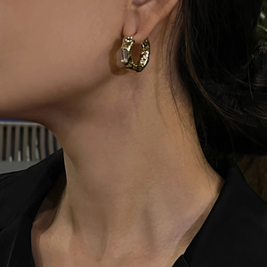 Close-up of golden geometric hoop earring with hammered texture and rectangle crystal
