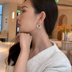 Close-up of silver C-shape hoop earrings with irregular lava texture on female model