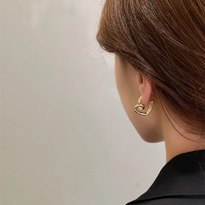 Minimalist golden heart spiral earrings for women worn by a model in a black suit