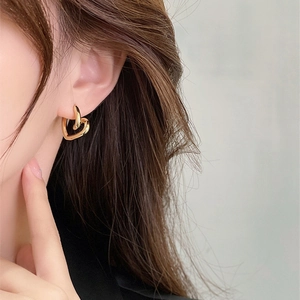 Polished gold heart-shaped interlocking drop earrings on model with high gloss finish