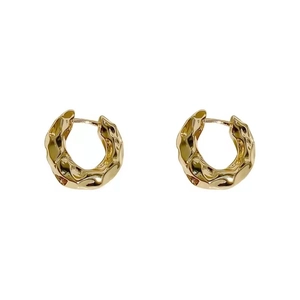 Minimalist gold hoop earrings with irregular hammered texture on a white background