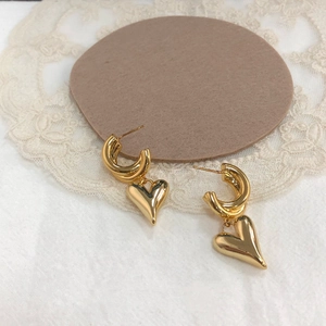 Détail de boucles d'oreilles cœur bombé doré avec maillons C sur dentelle blanche