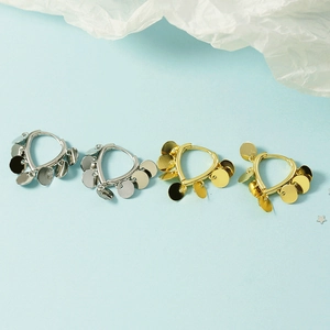 Minimalist gold and silver hoop earrings with shimmering circular metal charms on blue background