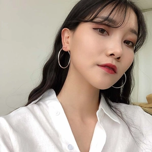 Close-up of minimalist large silver hoop earrings worn by a model in a white shirt