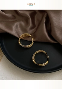 Detail shot of multi-layered gold hoop earrings on a black tray with silk fabric
