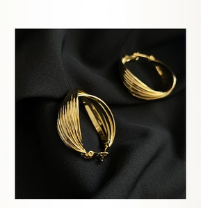 Detailed view of intertwined textured gold hoop earrings on elegant black fabric