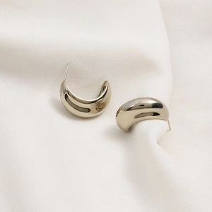 Golden crescent geometric earrings on white pleated chiffon background in soft light