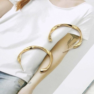 Detailed view of large gold twisted rope C-shaped hoop earrings with spiral metal texture