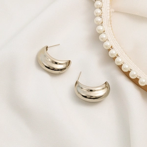 Minimalist C-shaped golden geometric metal earrings on white silk fabric background