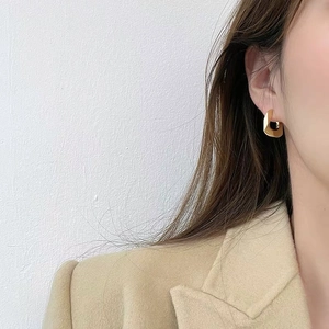 Close-up of golden geometric square earrings with polished metal finish on model